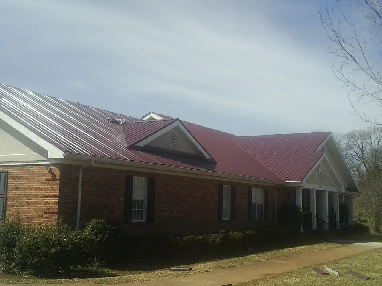 Red metal roof with gabled entries on a long brick building, from a Hail Damage Roof Repair job in Ninnekah