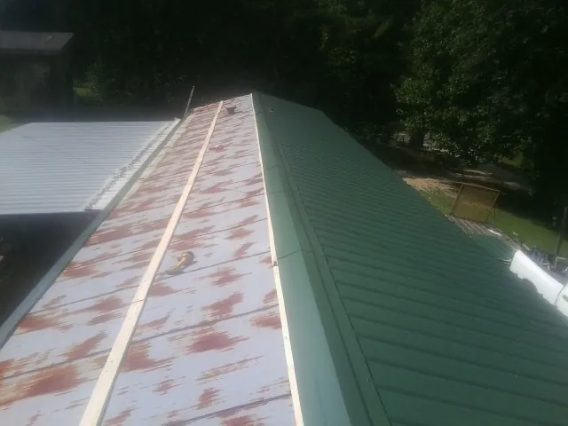 Old rusted panels beside newly installed green metal roofing — Wind Damage Roof Repair by Roofing Brothers in Ninnekah