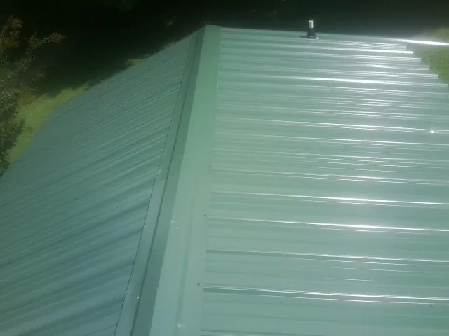 New green metal panels meeting at the ridge of a roof — Flat Roof Repair work by our crew in Ninnekah
