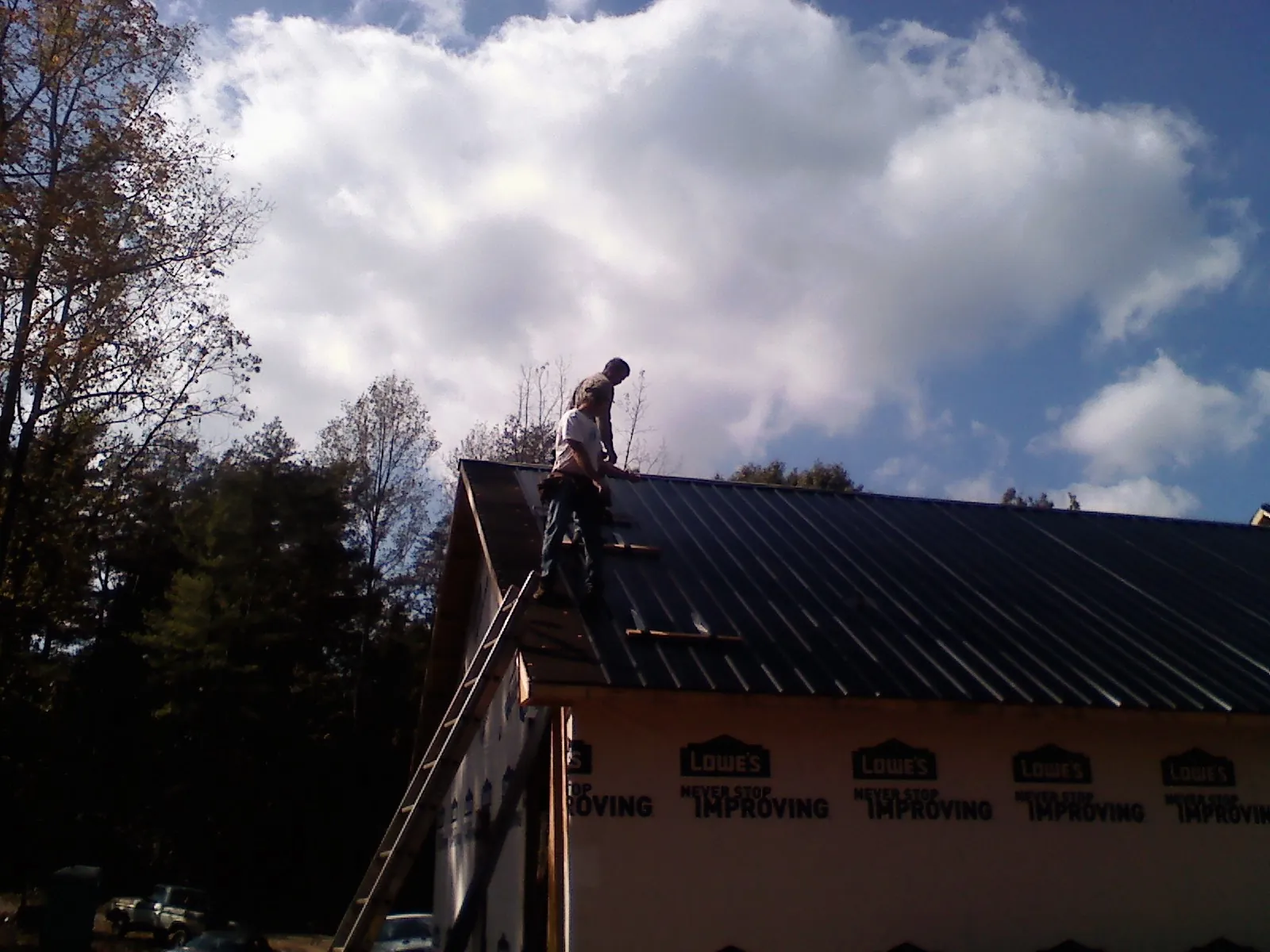 Roofer fastening dark metal panels high against a cloudy sky, from a Roof Inspection job in Ninnekah