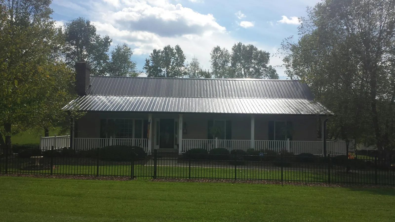 Gray metal roof on a brick ranch with a full width front porch — Gutter Guard Installation work by our crew in Ninnekah