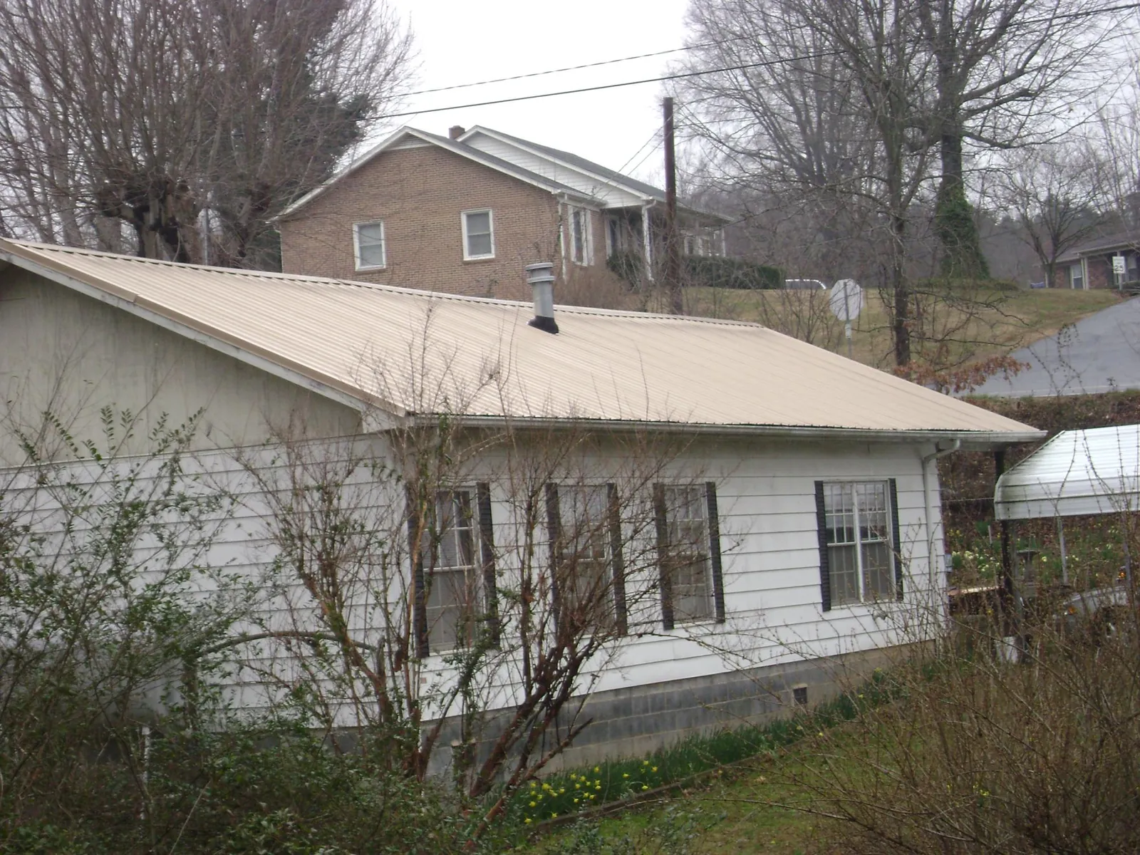 Tan metal roof on a white sided house set into a hillside — Commercial Roofing by Roofing Brothers in Ninnekah
