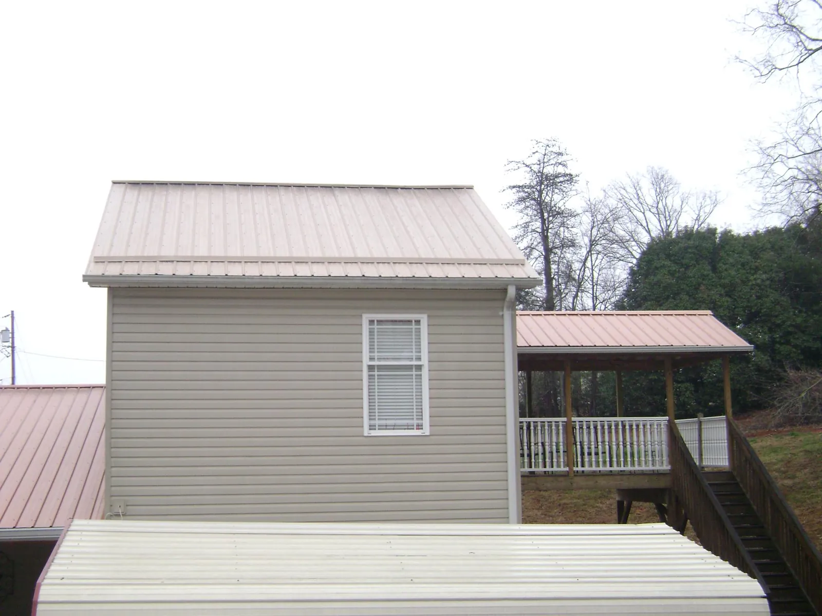 Tan metal roofs on a two story addition and attached porch, from a Roof Replacement job in Ninnekah